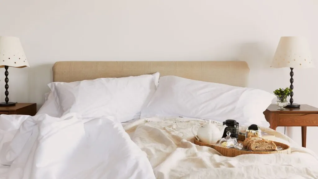 Large white half unmade bed with breakfast tray on top. Photograph taken in a villa in Portugal, Algarve