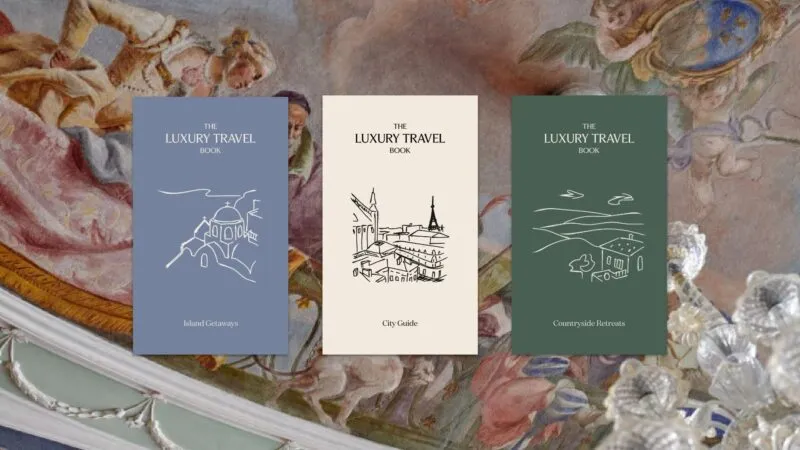 Three covers of leaflets of the same size present part of the offer of The Luxury Travel Book. All of them have the name of the company on the top, centred. The leftmost one is eggshell blue, with Greek Islands illustrated in the middle of the page and 'Island Getaways' written underneath, both in off-white. The one in the centre is off-white in colour, with a landscape of Paris and the Eiffel Tower illustrated in the middle of the page, and 'City Guide' written underneath, both in black. The rightmost one is a pastel forest green, with an Italian countryside landscape with a house illustrated in the middle of the page and 'Countryside Retreats' written underneath, both in off-white. A part of a Venetian fresco in one of the properties offered by The Luxury Travel Book is used as a background behind the leaflets.